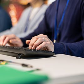 Manos con anillo teclean en un teclado, con una carpeta verde sobre la mesa